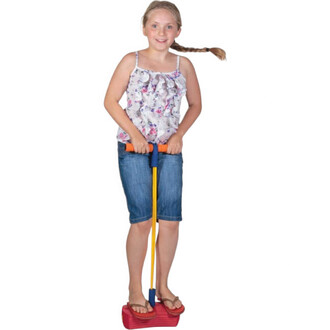 Fille souriante se tenant debout sur un Bungee Sauteur, portant un haut à fleurs et un short en denim. Elle tient la poignée du sauteur avec les deux mains et porte des sandales. Fond blanc.