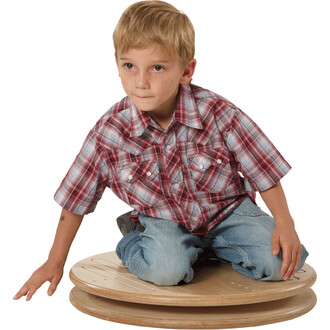 Un enfant assis sur le carrousel pour enfants Pedalo® 500, portant une chemise à carreaux rouges et un jean. Il est en train de jouer avec une expression concentrée.