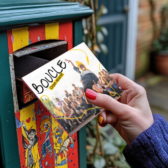 Une main tenant une brochure intitulée BOUCLE est insérée dans une boîte aux lettres colorée. En arrière-plan, une foule est réunie, tandis que la brochure montre un artiste en acrobatie. Le décor est vivant, avec des illustrations sur la boîte aux lettre