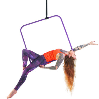 Cerceau aérien carré Prodigy utilisé par une artiste en position acrobatique, vêtue d'un haut orange et de leggings avec motifs galactiques, suspendue par un harnais, souriante, avec des cheveux longs et dégradés.