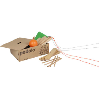 Caixa contendo elementos para o jogo em equipe Pedalo® 2, com uma caixa de papelão aberta mostrando acessórios de madeira, incluindo tábuas, um pequeno cone verde, uma bola laranja e cordas de diferentes cores.