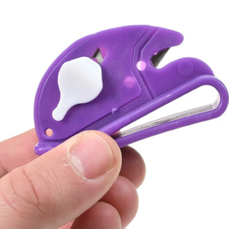Couteau coupe-ballons violet avec lame métallique partiellement sortie et protection blanche, tenu par une main.