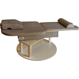 Table de massage avec un coussin pour la tête, revêtement en mousse beige, sur une base en bois circulaire.