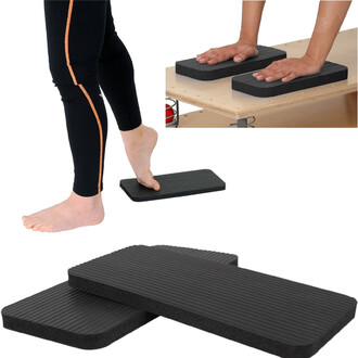 Image montrant un ensemble de deux planches noires en mousse pour la pratique de la jonglerie. Un pied nu est posé sur une des planches, tandis que deux mains reposent sur les autres planches situées sur une surface. Les planches ont une texture striée.