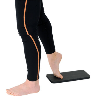 Un pied nu posé sur une plateforme noire. La personne porte un legging noir avec une bande orange sur le côté. La prise de vue se concentre sur la jambe et le pied, mettant en évidence l'utilisation de la plateforme.