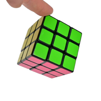 Cube casse-tête coloré, tourné en diagonale, avec des stickers verts, roses et jaunes, tenu par une main sur fond blanc.