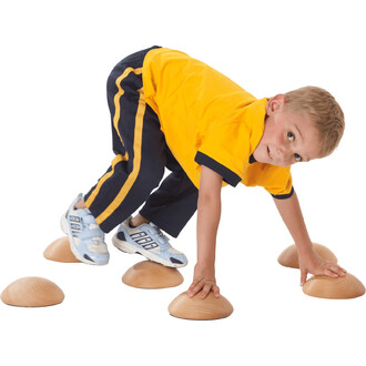 Un enfant en t-shirt jaune et pantalon bleu effectue un exercice de jonglerie en se tenant sur des cônes en bois. Il est à genoux et utilise une main pour s'appuyer sur un cône tout en levant une jambe pour en toucher un autre.