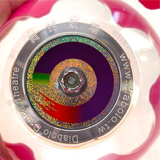 Diabolo Hyperspin à axe fixe – gros plan sur le disque coloré avec anneau holographique multicolore et l’axe central argenté sur fond rose.