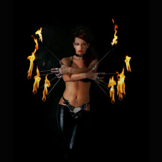 Femme performeuse en noir manipulant dix Doigts de feu Firetoys de 30 cm chacun, flammes jaillissant autour des mains sur fond noir.
