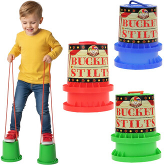 Un enfant souriant porte des échasses pieds d'éléphant colorées. Il est habillé d'un t-shirt jaune et de jeans, et se tient debout sur des seaux verts, en tenant des cordes reliées aux échasses. À l'arrière-plan, on peut voir des échasses rouges et bleues