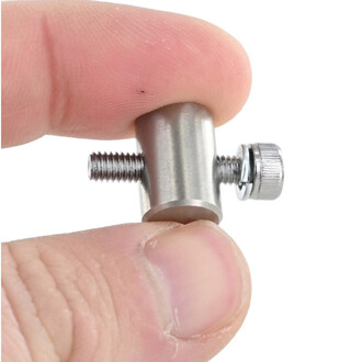 Écrou cylindre V3 en métal argenté avec filetage des deux extrémités et bague de serrage, vu en gros plan entre les doigts.