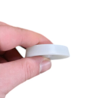 Embout haut blanc en forme de disque, petit accessoire en plastique tenu entre le pouce et l’index.