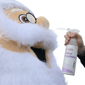 Mascotte en peluche blanche recevant le jet d’un embout spray depuis un flacon blanc étiqueté Odor Capturer.
