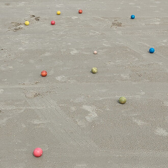 Balles de pétanque disposées sur un terrain sablonneux, avec des sphères de différentes couleurs : rouge, jaune, rose, bleu et vert, créant un contraste avec le sol beige.