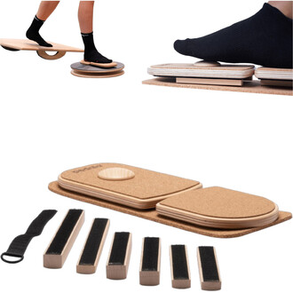 Plateau d'équilibre en bois avec plusieurs éléments, dont une base en liège et des parties mobiles pour travailler l'équilibre, accompagné de six petits blocs en bois et d'une sangle pour l'utilisation. Deux pieds en chaussettes noires posés sur les planc