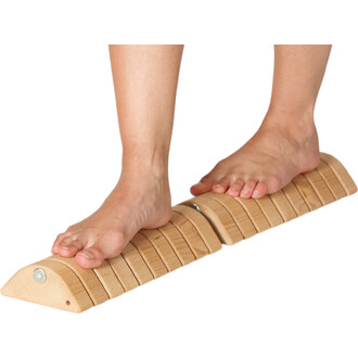 Deux pieds nus sont posés sur un accessoire d'entraînement en bois, qui présente une surface légèrement inclinée avec des rainures. Cet outil est conçu pour améliorer l'équilibre et la stabilité.