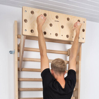 Homme en train de s'entraîner sur une poutre avec préhensions en bois, les mains tenant des prises, vue de dos. Mur blanc en arrière-plan avec une structure en bois.