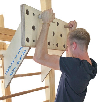 Homme effectuant un exercice sur un espalier Pedalo® Line, tenant une plaque en bois avec des trous et des poignées. Le texte Adaptateur non inclus est visible sur la plaque. En arrière-plan, on aperçoit les barres en bois de l'espalier.