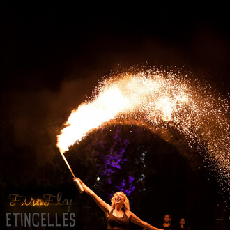 Artiste de feu en action, tenant une torche produisant une traînée d'étincelles lumineuses dans une nuit noire, créant une atmosphère festive et dynamique.