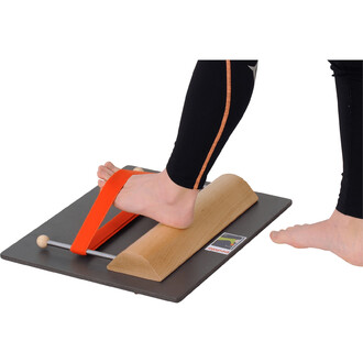 Image d'un pied sur un dispositif de jonglerie Foot Workshop S7 Pedalo®. Le pied est maintenu par une sangle orange, tandis qu'une partie en bois en forme de rouleau est visible sous le pied. L'ensemble est posé sur une plateforme noire. La scène met en a