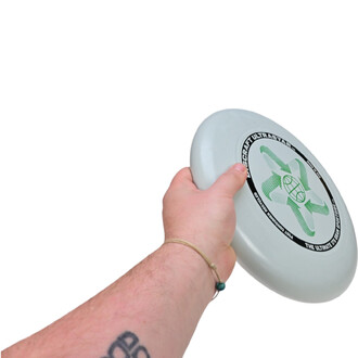 Main tenant un frisbee Ultrastar phosphorescent de la marque Discraft, avec un décor central en vert sur un fond blanc. La forme arrondie et lisse du frisbee est bien visible, montrant sa surface plane et ses motifs.