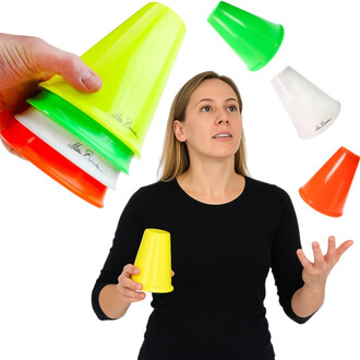 Une personne jonglant avec des gobelets colorés, dont un jaune et un orange, tandis que d'autres gobelets verts, rouges et blancs flottent autour d'elle. Elle a une expression concentrée et porte un t-shirt noir. Un bras tient une pile de gobelets.