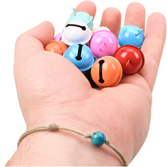 Grelots colorés de 22 mm tenus dans une main, comprenant des teintes variées comme bleu, orange, rouge, rose et vert, avec un bracelet en corde sur le poignet.