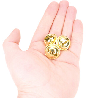 Grelots plats de 22 mm en couleur or, posés sur la paume d'une main. Trois grelots brillants visibles, montrant leur surface réfléchissante et leur design arrondi. Fond blanc.