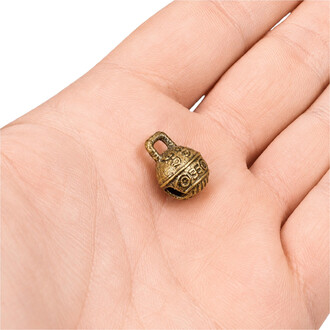 Grelot tibétain miniature en métal bronze vieilli avec motifs gravés et boucle en haut, diamètre environ 11 mm, posé sur la paume d'une main.