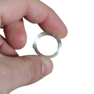 Plan rapproché d’un petit anneau métallique tenu entre les doigts, montrant l’intérieur rainé et la surface brute.