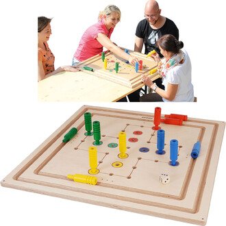 Trois personnes jouent autour d'une table avec un jeu de société, affichant un plateau en bois clair avec des pions colorés (rouge, jaune, bleu et vert) disposés sur un maillage de trous. Le plateau est orné de motifs circulaires et comporte un dé. Une de