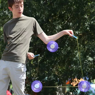 Jeune jongleur s'exerçant avec trois diabolos Typhoon de couleur violette, manipulant des baguettes en aluminium anodisées. L'arrière-plan est rempli de feuillage verdoyant, créant une atmosphère dynamique.