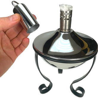 Lampe à huile torchière en métal chromé avec mèche blanche; une main tient le bouchon métallique amovible prêt à être inséré sur le sommet de la lampe.