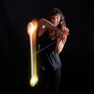 Une personne en train de jongler avec un Levistick Lumi Pro LED, montrant des mouvements dynamiques. Le bâton lumineux est au centre de l'image, émettant des lumières colorées. L'arrière-plan est noir, mettant en valeur l'éclat du produit. La personne por