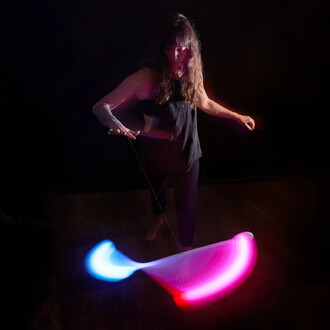 Une personne jongle avec un Levistick Lumi Pro LED, créant des traînées de lumière rouge et bleue dans un environnement sombre. Elle se tient debout, pieds nus, en tenant le bâton avec une main, tandis que l'autre main est levée pour le contrôle.