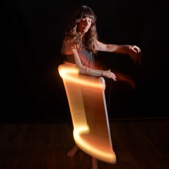 Une performeuse de jonglerie utilise le Levistick Lumi Pro LED, créant des effets lumineux en mouvement dans une ambiance sombre. L'image montre des traînées de lumière orange qui se déplacent autour d'elle, mettant en valeur la fluidité de ses mouvements