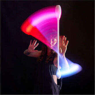 Femme en train de jongler avec un Levistick Lumi Pro LED, créant des traînées lumineuses colorées dans l'obscurité. Ses mains sont levées, et des lumières vives en rose et bleu se dessinent derrière elle.