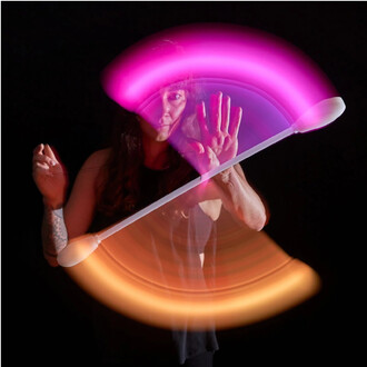Image d'un artiste manipulant le Levistick Lumi Pro LED, avec des lumières violettes et orange créant des traînées lumineuses autour de lui. La personne est en action, avec une main levée et une expression concentrée. Fond noir pour mettre en valeur l'eff
