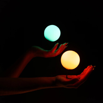 Deux mains tiennent des palets lumineux : un palet émettant une lumière verte et un autre une lumière orange, le tout sur un fond noir.