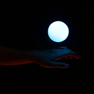 Main élégante tendue vers une sphère lumineuse bleue dans un espace sombre, avec un contraste de couleurs qui met en valeur le mouvement et l'éclat de la lumière.