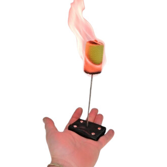 Main de Feu Confort tenue dans une main, avec un bâton en métal supportant une flamme. Le haut du bâton est recouvert d'une tête en tissu coloré, orange et jaune, qui brûle. Le fond est une base noire avec des rivets, soulignant l'utilisation d'accessoire