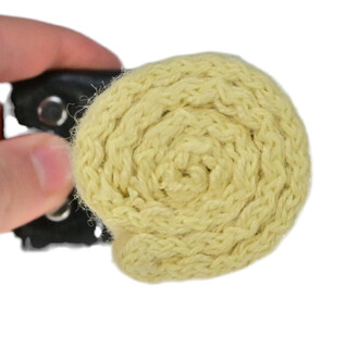 Main de Feu Confort, présentant une tête en tissu jaune enroulée, tenue par une main avec un bracelet noir en arrière-plan.