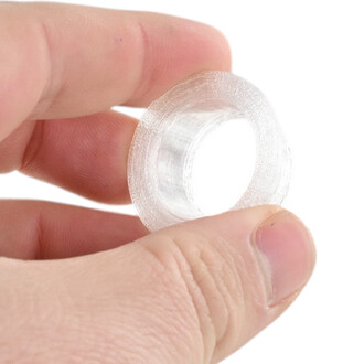 Gros plan d'un manchon Prism transparent en plastique, tenu entre le pouce et l'index, montrant un anneau mince avec des stries internes.
