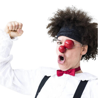 Personne déguisée en clown avec des cheveux frisés, portant un chapeau noir. Elle a deux nez rouges en silicone sur le visage, un sur le nez et un autre sur le front. La personne exprime une grande émotion, avec un poing levé et la bouche ouverte dans un 