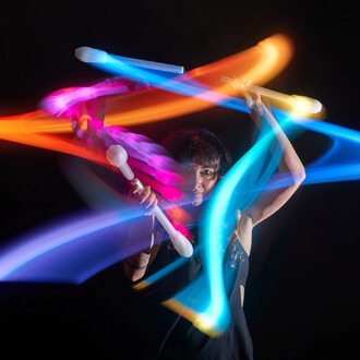 Jeune femme utilisant des nunchakus lumineux LED, créant des traînées de couleurs vives dans une ambiance sombre. Les nunchakus émettent des lumières rouge, bleue, et rose, tandis que la femme semble concentrée sur sa performance de jonglage.