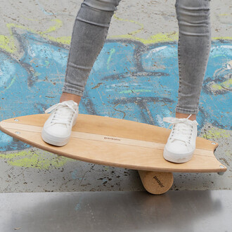 Une personne se tiens debout sur une planche en bois, équilibrée sur un cylindre en liège. Elle porte des baskets blanches et un jean gris, avec un fond coloré de graffiti.