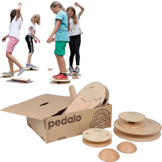 Enfants s'amusant sur des équipements de jonglerie Pedalo® Balance-Box, avec des planches en bois et différents éléments de déséquilibre, tandis qu'une boîte en carton est ouverte à côté, montrant les pièces à l'intérieur.