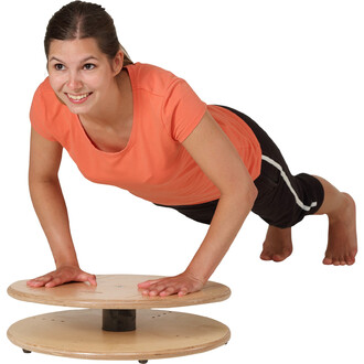 Femme en position de planche sur un appareil de fitness en bois, souriante, portant un t-shirt orange et un short noir.