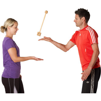 Une femme en t-shirt violet et un homme en t-shirt rouge se tiennent face à face, avec la main de l'homme tendue vers l'avant, lançant un bâton en bois qui flotte au-dessus de la paume de la femme. Ils semblent concentrés sur l'objet en l'air.