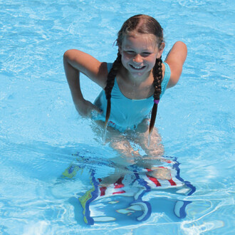 Fille souriante dans une piscine, portant un maillot de bain bleu, s'amusant sur un Pedalo® Classique S Aqua coloré, avec des éclaboussures d'eau autour d'elle.